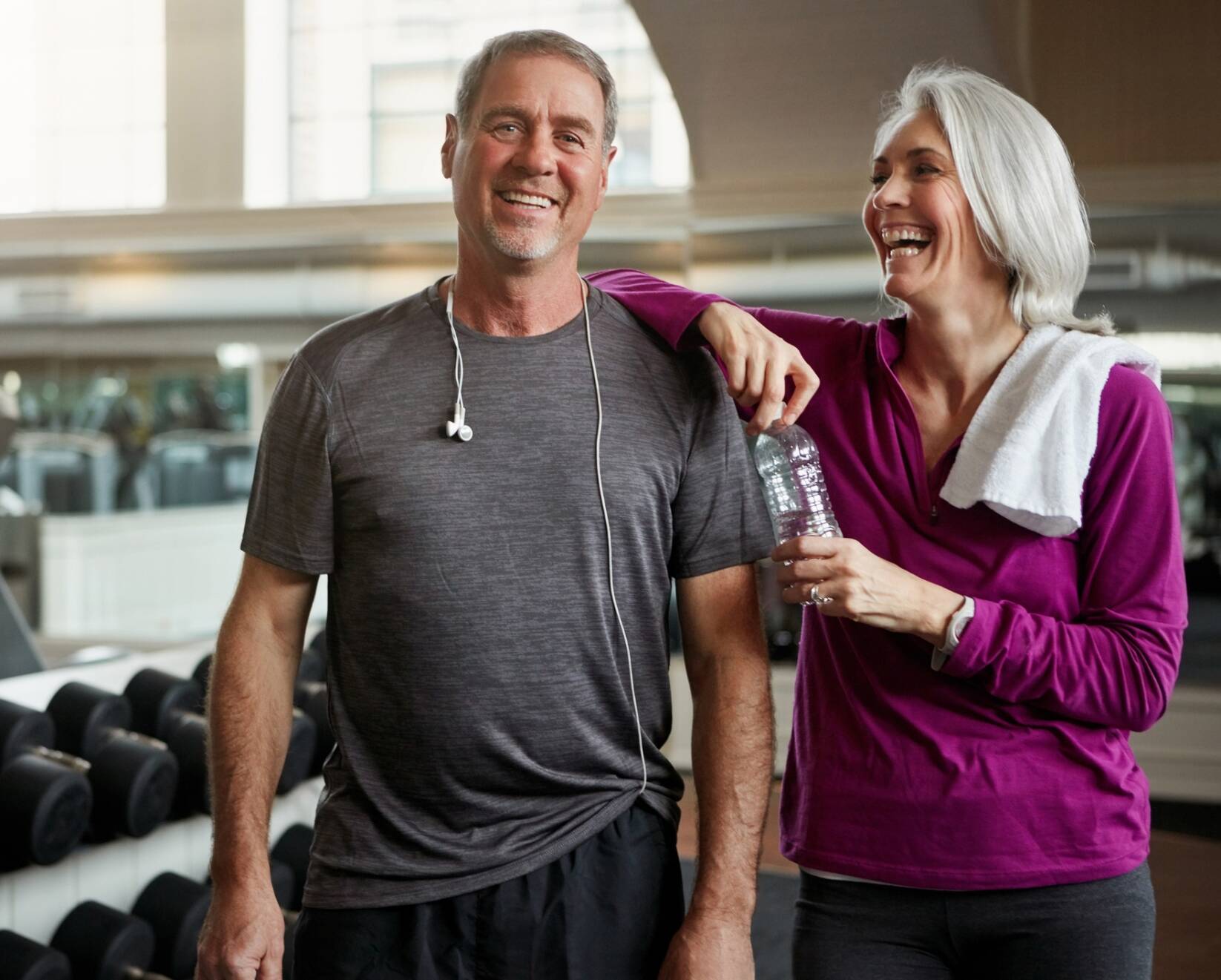Shot of a senior married couple laughing and taking a break from their workout at the gym
