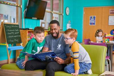 YMCA teacher sitting in chair reading to elementary age students in classroom